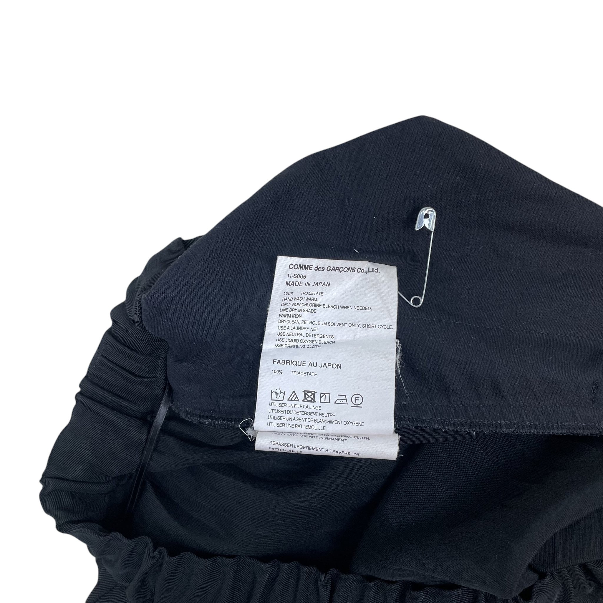 Zenno Archive Comme des Garcons BLACK pleated skirt care label with safety pin on a textured background